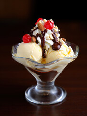 A vanilla ice cream sundae with chocolate sauce cherries and nuts in a glass dessert bowl on a table
