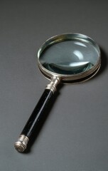 A magnifying glass with a dark, likely black, wooden handle and a silver-colored metal frame