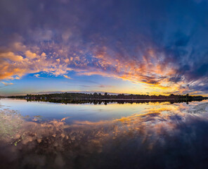 Awesome sunset on sky and reflected in the water river Soft pink clouds of warm and cool tones play images on canvas. Dramatic evening light and fiery orange violet sunset. Yellow fire blue background