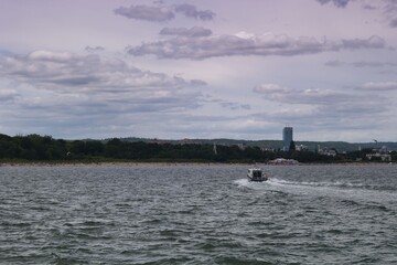 Boat navigates through cloudy waters near a coastal city under a pastel sky at dusk
