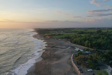 Aerial drone photo of a tropical ocean coastline with a wide sandy beach illuminated by warm golden sunset light