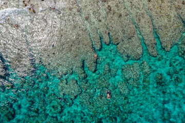 Aerial top-down view of a vibrant ocean reef with crystal turquoise water, where people are swimming and exploring
