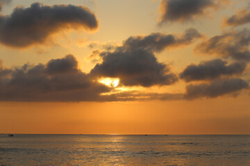 Fototapeta premium Ocean panorama with cloudy orange sky and setting sun through the clouds