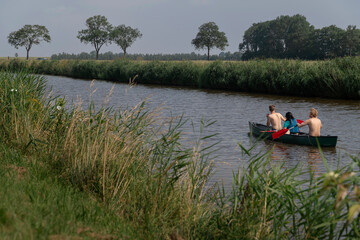 People paddling canoe through scenic waterway surrounded by reeds and countryside