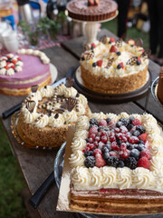 Variety of decorated layer cakes with berries and cream on outdoor wooden table