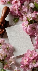 Blank card surrounded by delicate pink blossoms and a wooden stamp