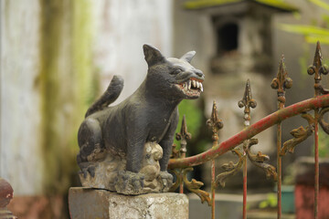 A small stone sculpture of a dog with exaggerated large teeth standing on an elevated platform near...