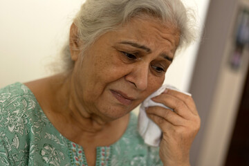 Aged old woman is weeping and crying away tears. Senior lonely woman sitting at home and looking away at home
