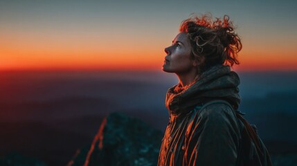 Woman looking up at a vibrant sunset sky during a mountain hike, feeling inspired and contemplative