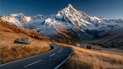 Scenic mountain road winding through a valley with snowcapped peaks and golden autumn foliage under a clear blue sky