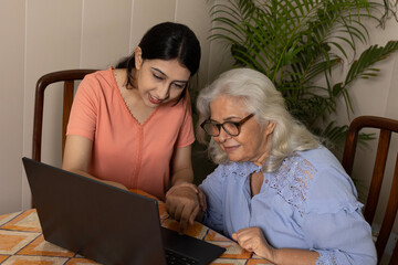 Indian young granddaughter taking care of grandmother at home helping her in learning online deliveries and payments by using laptop in living room