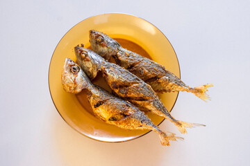 A delicious platter of three deep-fried Mackerel fish, crispy and golden-brown. Served on a transparent brown glass plate, this appetizing shot highlights Asian cuisine, fresh seafood, and home cook
