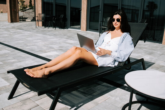 Relaxing woman working on laptop by the poolside in modern outdoor setting