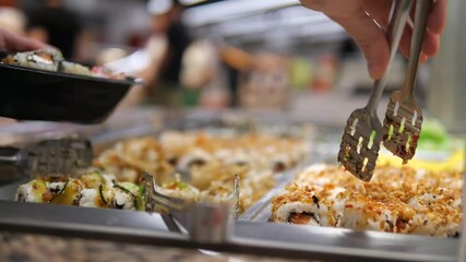 Hands carefully select sushi pieces into a container at a unlimited dining setting, evoking luxury and variety. Great for travel vlogs, restaurant promotions, or lifestyle content.