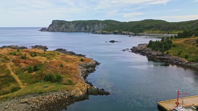 A drone glides over Brigus South serene bay, capturing a grassy headland and rocky shoreline meeting calm waters and distant cliffs along Newfoundlands rugged coast.
