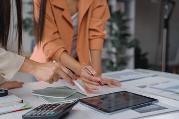 Two businesswomen are collaborating on a project, analyzing financial data displayed on a digital...