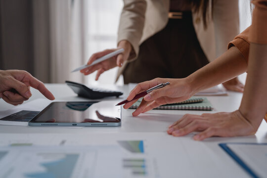 Business colleagues are collaborating and reviewing financial statistics displayed on a digital tablet, using a pen to point at specific data points and discuss growth opportunities