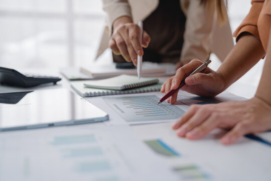 Business people collaborating in an office, analyzing financial charts and graphs with pens in hand. Utilizing calculators, tablets, and notebooks to strategize and plan for growth