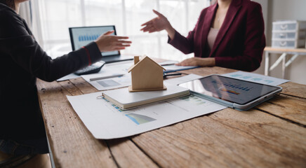 Real estate agent showing house model to client discussing mortgage loan terms and interest rates, property insurance, purchase agreement, and housing market analysis