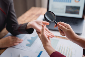 Two businesswomen are using a magnifying glass to carefully examine financial charts and graphs, seeking insights and making informed decisions for their business