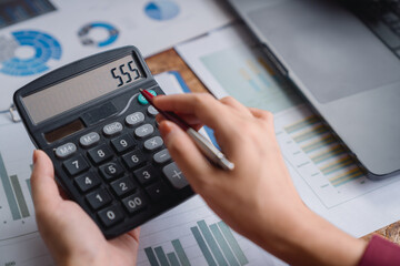 Accountant is calculating and checking financial data graphs, using calculator and pen, working with financial documents, business accounting concept