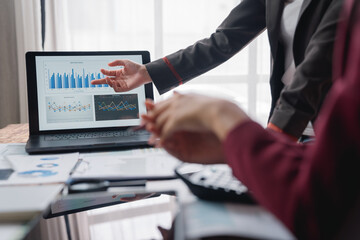 Business professionals discussing sales performance while analyzing charts displayed on a laptop screen during a meeting in a modern office environment, fostering collaboration and strategy