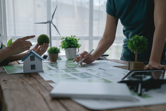 Two engineers are discussing an eco-friendly house project with solar panels and a wind turbine, promoting sustainable and green building practices for a better future