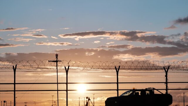Airport security patrol driving along perimeter fence at sunset