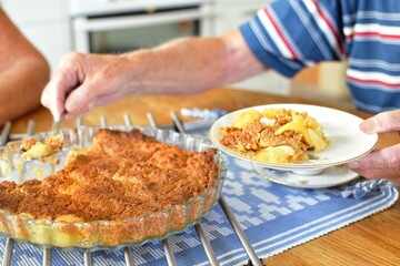 There is Swedish apple pie on the table, an elderly man puts the pie on his plate. Pie and fika.
