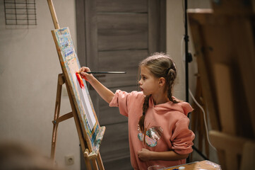 Girl enjoys painting in workshop. Art lesson. Education and learning concept. Child draw a picture in art class. School kid drawing with brush landscapes on easel. Mix and combine colors.