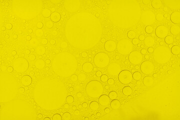 Macro abstract image of golden oil bubbles suspended in liquid, forming overlapping circular patterns. The texture and light create a warm, artistic background perfect for cosmetic, beauty