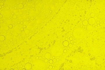 Macro abstract image of golden oil bubbles suspended in liquid, forming overlapping circular patterns. The texture and light create a warm, artistic background perfect for cosmetic, beauty