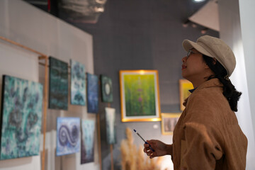 Woman observing artwork in modern art gallery. Captures moment of thoughtful appreciation, ideal for themes of creativity, inspiration, education, and cultural exploration.