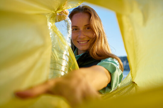 Smiling volunteer putting plastic bottles in yellow garbage bag