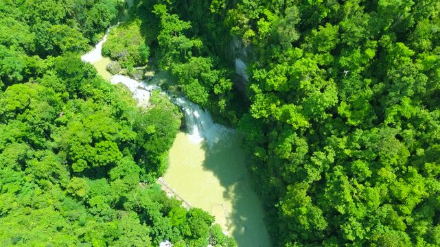 Aerial view of the multi-tiered waterfall and river flowing through a lush tropical forest, Kawasan Falls, Cebu, Philippines.