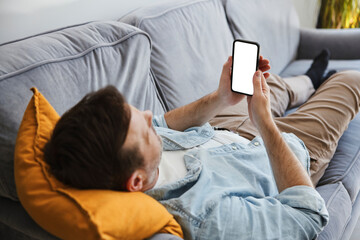 Person relaxing at home on sofa using smartphone with blank screen