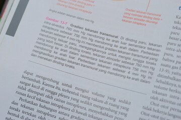 Obraz premium A close-up of an open medical textbook, showing detailed text and diagrams about human physiology and biology. This image represents study, education, research, and the journey of a medical student.