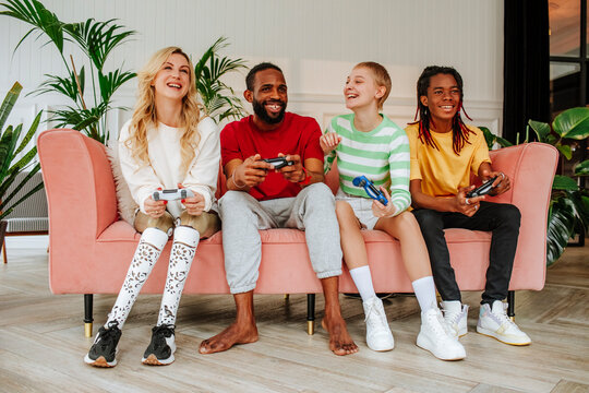 Friends enjoying video game sitting together on sofa at home