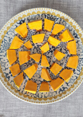 Pieces, cubes of pumpkin on porcelain plate with blue pattern. Farm products and healthy eating. Kitchen and home cooking.