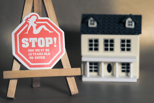 Red stop sign with age restriction on easel in front of model house, symbolizing privacy, boundaries, and adult-only access.