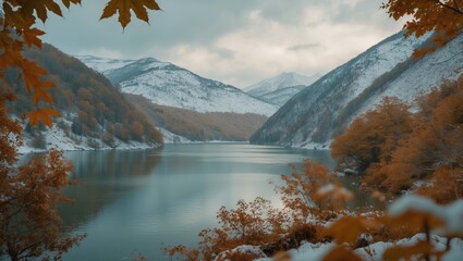Autumn landscape of mountains and lake with snow-capped peaks and orange foliage. Mountain scenery in fall with calm water and forested slopes.