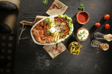 Traditional Turkish Doner Kebab Plate with Fresh Vegetables, French Fries, and Sauces on Rustic Background