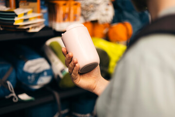 Hand holding pink thermal travel mug in camping equipment store.