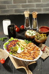 Traditional Turkish Doner Kebab Plate with Fresh Vegetables, French Fries, and Sauces on Rustic Background