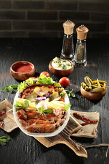 Traditional Turkish Doner Kebab Plate with Fresh Vegetables, French Fries, and Sauces on Rustic Background