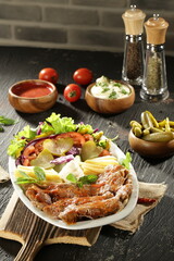 Traditional Turkish Doner Kebab Plate with Fresh Vegetables, French Fries, and Sauces on Rustic Background