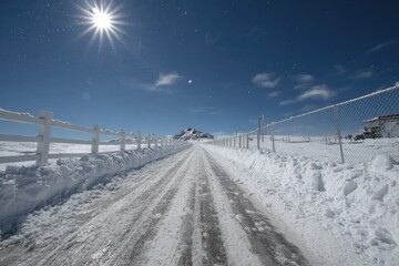 Snowy road leading to a mountain under a bright sun
