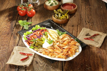 "Traditional Turkish Doner Kebab Plate with Fresh Vegetables, French Fries, and Sauces on Rustic Background"