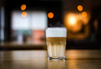 Close-up of a hot latte macchiato in a tall transparent glass, resting on a wooden table in a cozy café or restaurant setting warm, inviting, and elegantly layered, dark light.