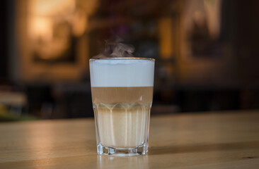 Close-up of a hot latte macchiato in a tall transparent glass, resting on a wooden table in a cozy café or restaurant setting warm, inviting, and elegantly layered, dark light.